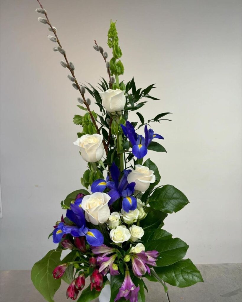 Tall arrangement of ivory roses and blue iris with bells of Ireland