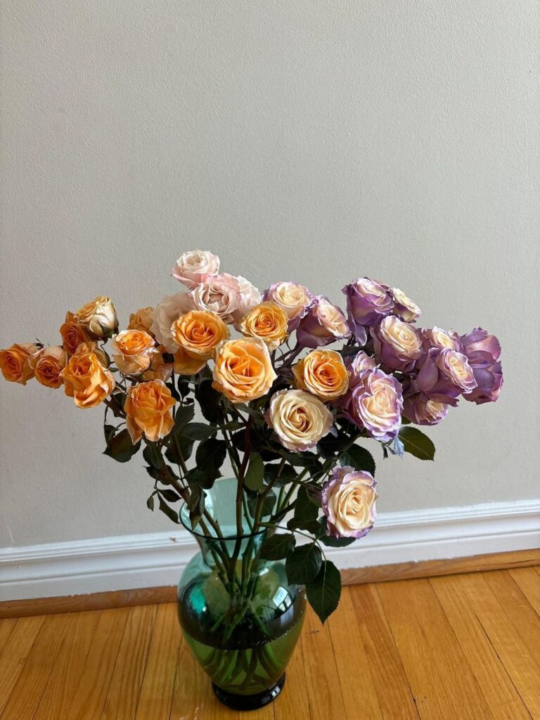 Peach, blush and lavender-edged roses arranged loosely in a green glass vase