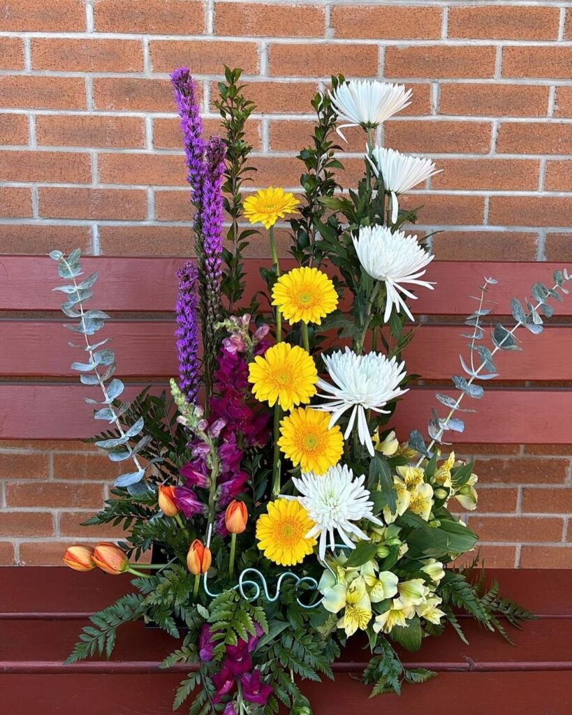 Garden arrangement of gerberas, spider mums and liatris against a brick wall